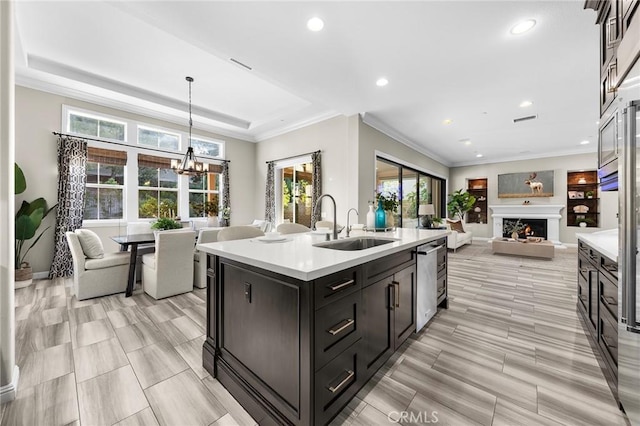 kitchen with sink, a chandelier, decorative light fixtures, a center island with sink, and ornamental molding