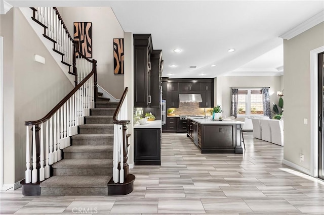 kitchen with crown molding, a breakfast bar area, decorative backsplash, a center island with sink, and dark brown cabinets