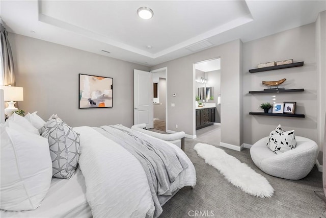 carpeted bedroom featuring a raised ceiling and ensuite bath