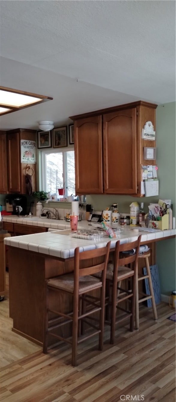 kitchen with a kitchen breakfast bar, kitchen peninsula, tile counters, and light wood-type flooring