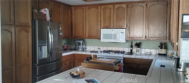 kitchen with brown cabinets, white microwave, tile counters, and stainless steel refrigerator with ice dispenser