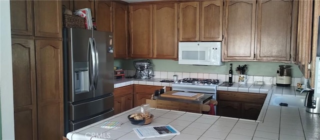 kitchen featuring white appliances, brown cabinetry, tile countertops, a peninsula, and a sink