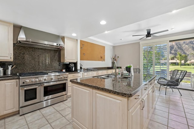 kitchen with tasteful backsplash, a kitchen island with sink, range with two ovens, wall chimney exhaust hood, and sink