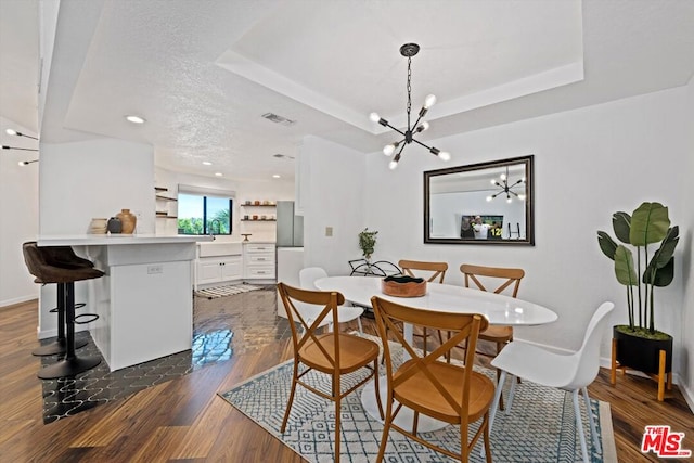 dining space featuring a raised ceiling, a chandelier, dark hardwood / wood-style flooring, and a textured ceiling