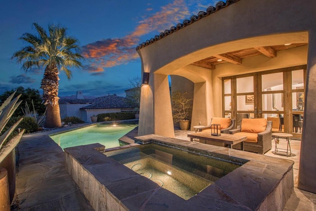 pool at dusk with an in ground hot tub, a patio, and an outdoor hangout area