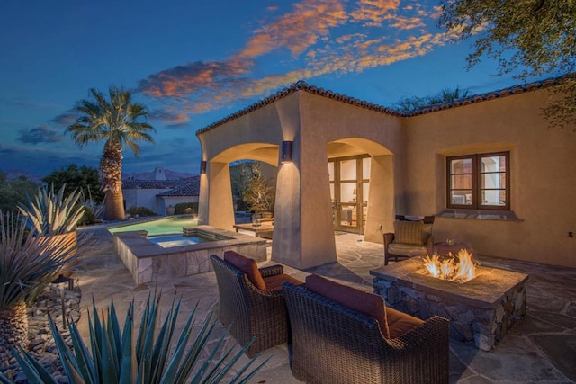 patio terrace at dusk featuring an in ground hot tub and a fire pit