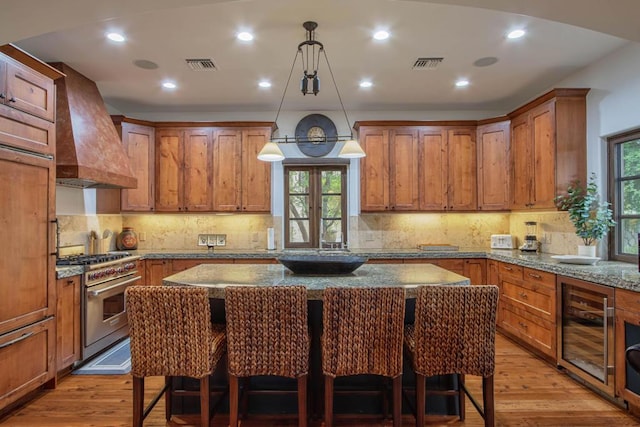 kitchen with a wealth of natural light, wine cooler, premium range hood, and stainless steel stove