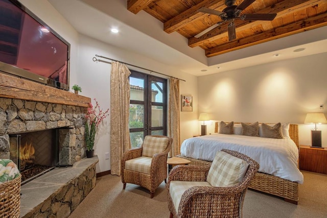 bedroom featuring a stone fireplace, ceiling fan, beam ceiling, light colored carpet, and wood ceiling