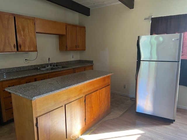 kitchen with beam ceiling, sink, stainless steel fridge, a center island, and light wood-type flooring