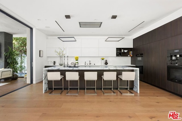 kitchen with light hardwood / wood-style floors, white cabinetry, and a kitchen breakfast bar