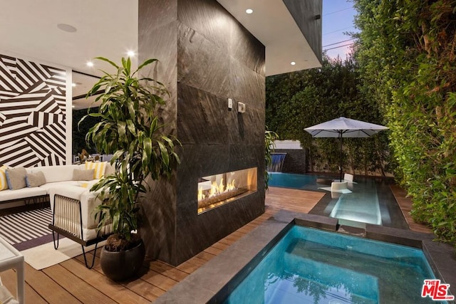 pool at dusk featuring an in ground hot tub, a deck, and an outdoor living space with a fireplace