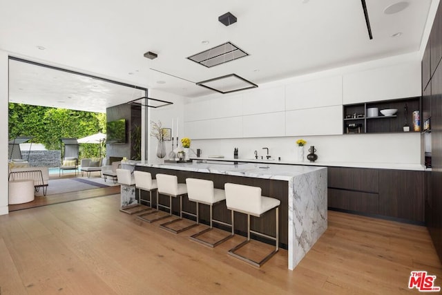 kitchen featuring a kitchen island, a kitchen breakfast bar, white cabinetry, light hardwood / wood-style flooring, and light stone counters