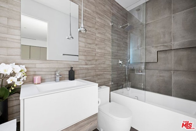 full bathroom with decorative backsplash, toilet, vanity, tile walls, and combined bath / shower with glass door