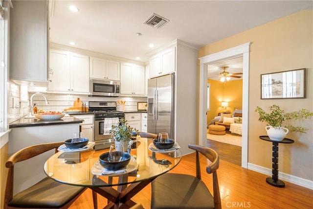 kitchen with white cabinets, ceiling fan, backsplash, light hardwood / wood-style floors, and stainless steel appliances