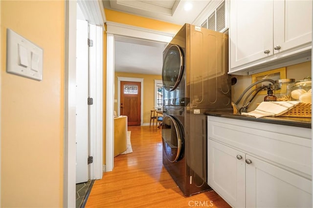 laundry room with stacked washer / dryer, light wood-type flooring, and cabinets