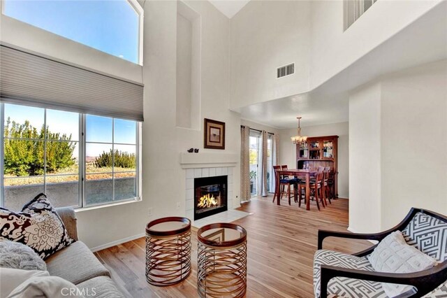 living room with a tile fireplace, a towering ceiling, a notable chandelier, and light wood-type flooring