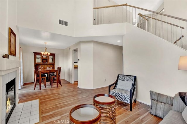 living room featuring a tile fireplace, a towering ceiling, and light hardwood / wood-style floors