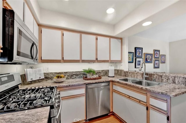 kitchen with sink, light hardwood / wood-style flooring, kitchen peninsula, white cabinets, and appliances with stainless steel finishes