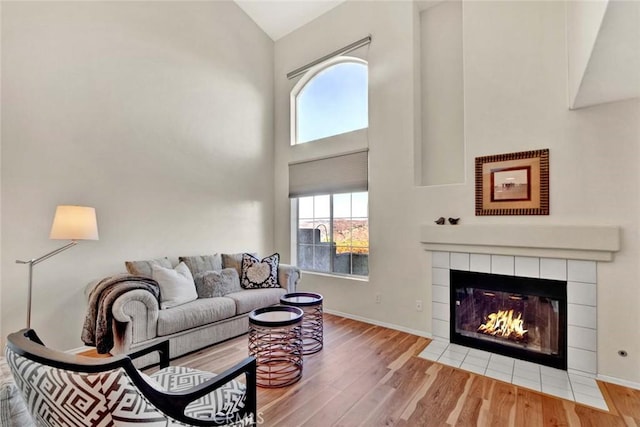 living room featuring wood-type flooring, high vaulted ceiling, and a tiled fireplace