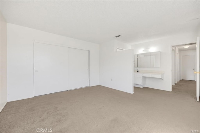 unfurnished bedroom with a closet, built in desk, connected bathroom, and light colored carpet