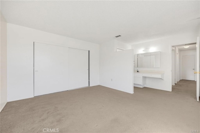 unfurnished bedroom featuring a closet, light carpet, built in desk, and ensuite bathroom