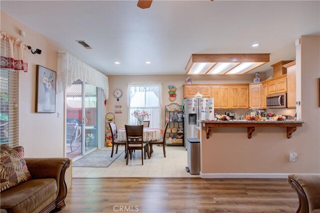 kitchen with a breakfast bar area, light hardwood / wood-style flooring, light brown cabinets, appliances with stainless steel finishes, and kitchen peninsula