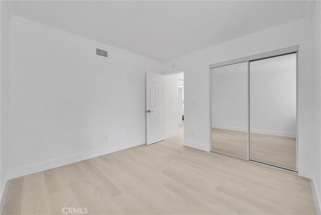 unfurnished bedroom featuring light wood-type flooring, crown molding, and a closet