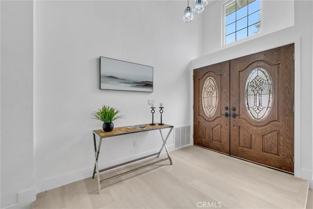 foyer featuring french doors, a towering ceiling, and light hardwood / wood-style floors