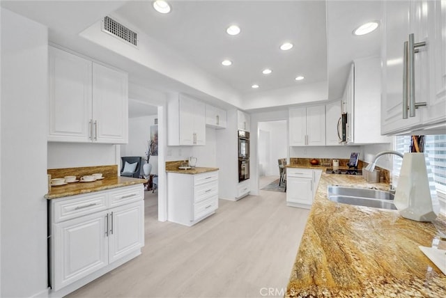 kitchen featuring light stone counters, sink, white cabinets, and light wood-type flooring