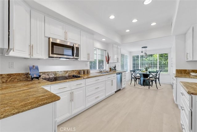 kitchen with appliances with stainless steel finishes, light wood-type flooring, sink, pendant lighting, and white cabinetry