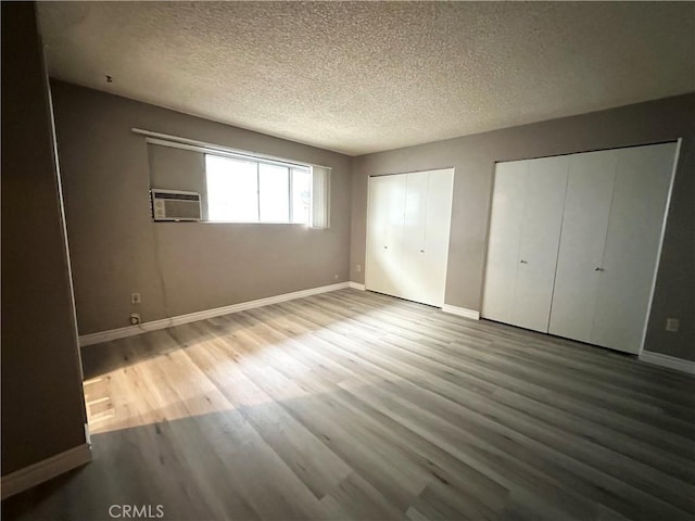 unfurnished bedroom with wood-type flooring, a wall unit AC, a textured ceiling, and two closets