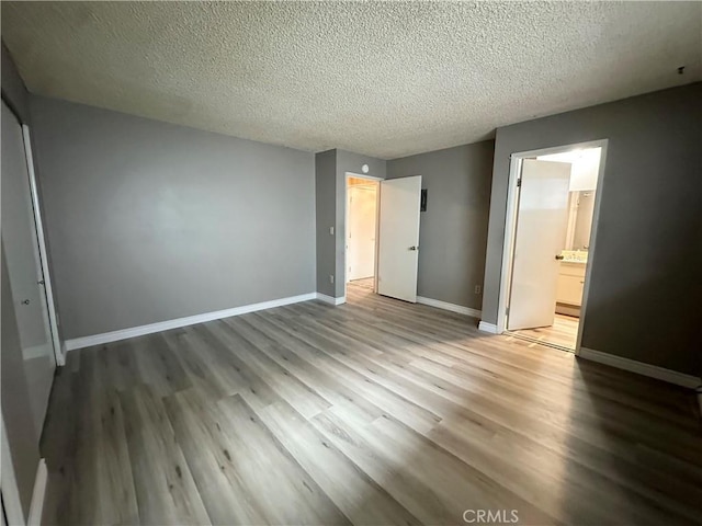 unfurnished bedroom with baseboard heating, a textured ceiling, ensuite bath, a closet, and hardwood / wood-style flooring