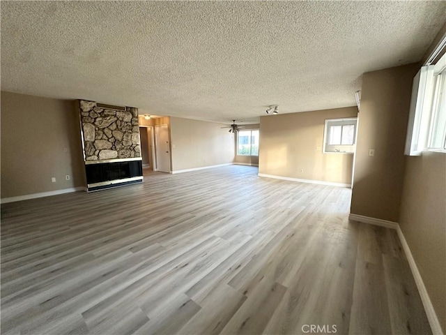 unfurnished living room with a textured ceiling, ceiling fan, light hardwood / wood-style floors, and a fireplace