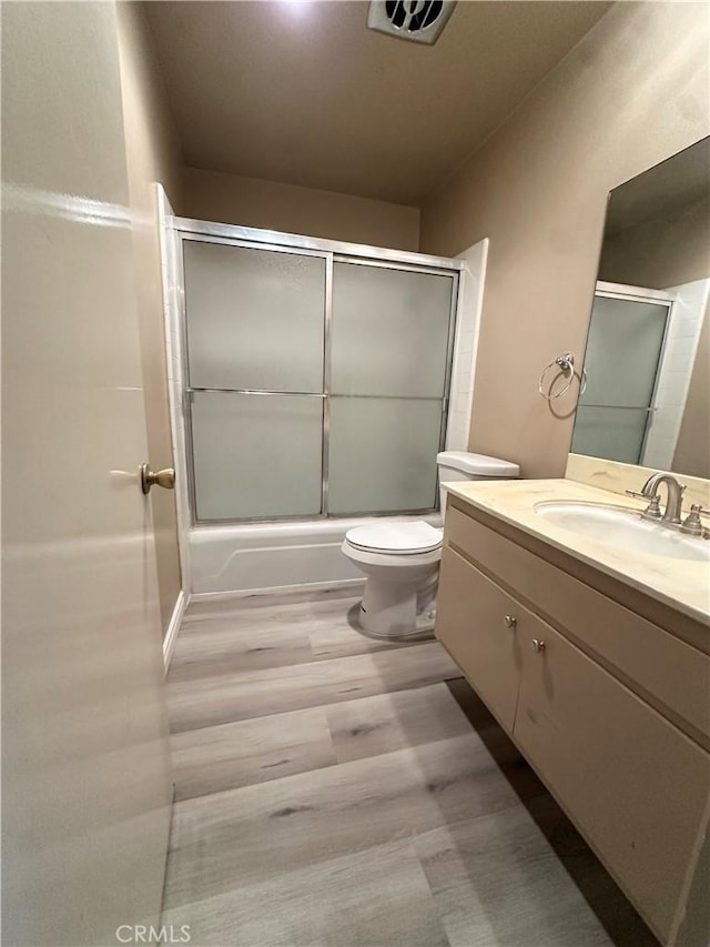 full bathroom featuring toilet, bath / shower combo with glass door, wood-type flooring, and vanity