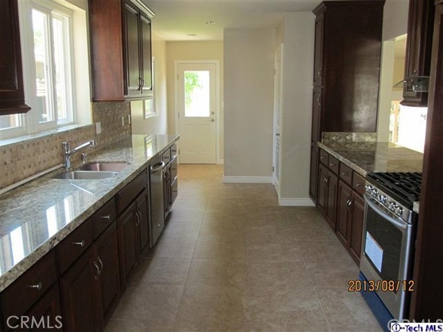 kitchen featuring stainless steel appliances, sink, light stone countertops, light tile patterned floors, and tasteful backsplash