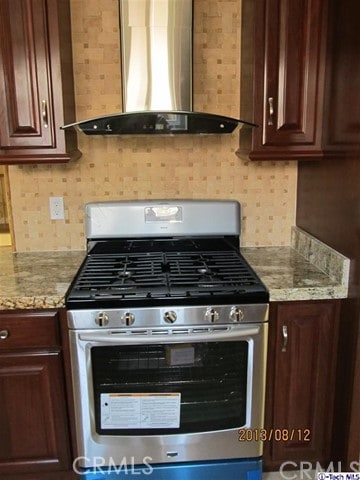 kitchen with dark brown cabinetry, stainless steel range with gas cooktop, light stone counters, and range hood