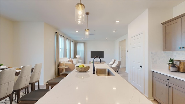 kitchen with decorative backsplash, hanging light fixtures, sink, and light stone counters