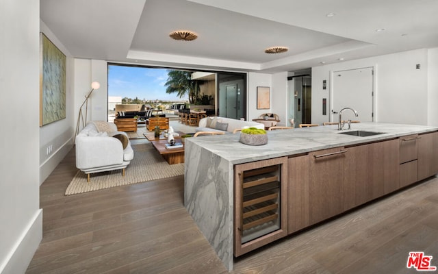 kitchen featuring a kitchen island with sink, dark wood-type flooring, wine cooler, sink, and a raised ceiling