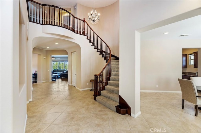 tiled foyer with a towering ceiling and ceiling fan with notable chandelier