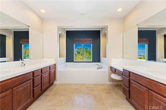 bathroom with a relaxing tiled tub, vanity, and tile patterned floors