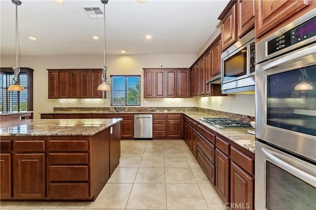 kitchen featuring stainless steel appliances, decorative light fixtures, a center island, and light stone countertops