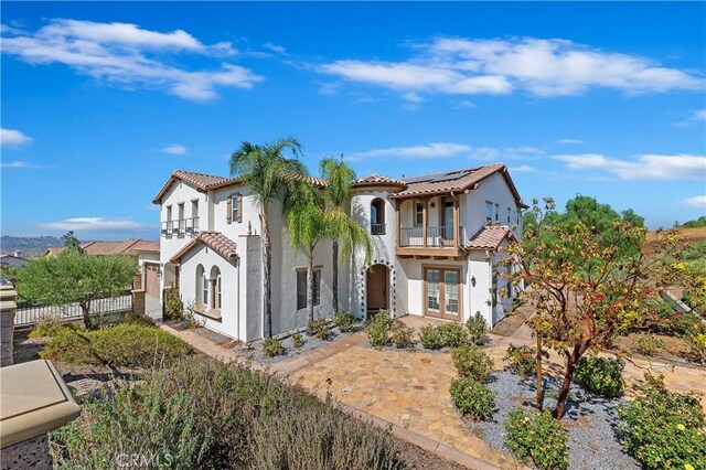 mediterranean / spanish-style home featuring french doors, solar panels, and a balcony