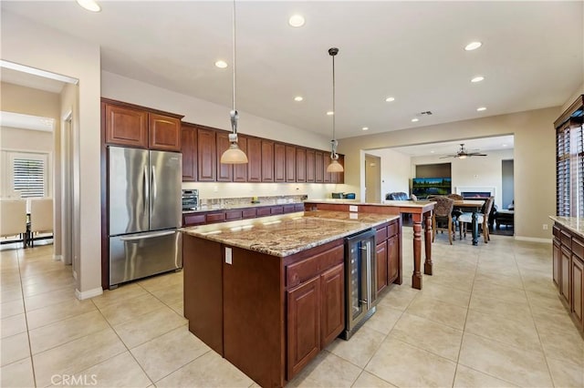 kitchen with wine cooler, light stone counters, a center island, stainless steel refrigerator, and pendant lighting