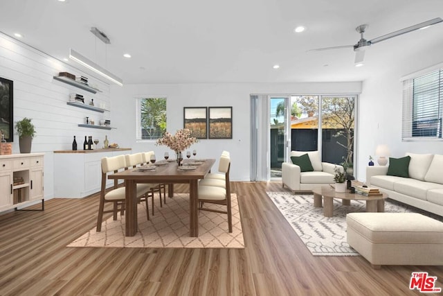 dining room with ceiling fan, wooden walls, and light hardwood / wood-style flooring