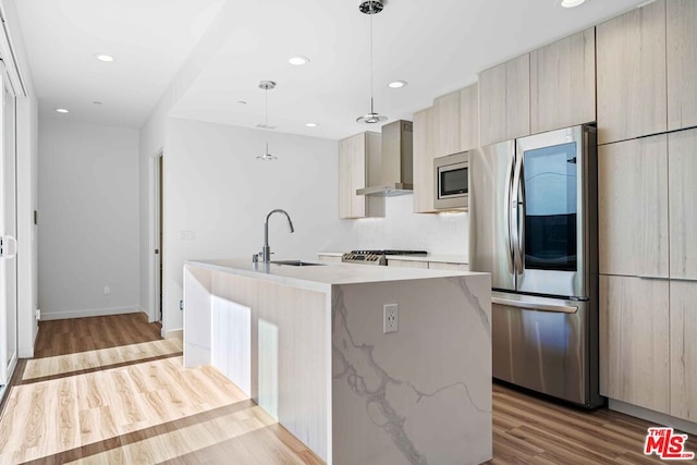 kitchen with stainless steel appliances, a kitchen island with sink, sink, wall chimney range hood, and light hardwood / wood-style floors