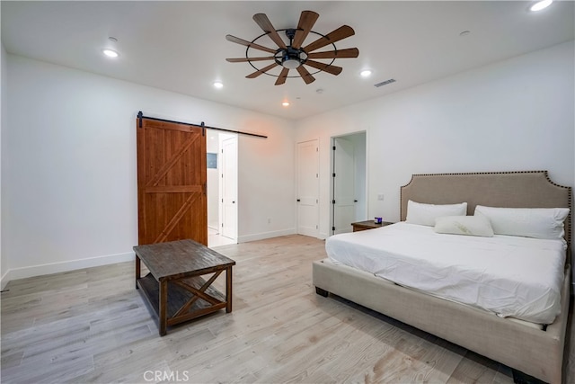 bedroom featuring a barn door, light wood-type flooring, and ceiling fan