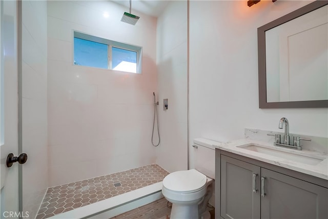 bathroom featuring vanity, toilet, wood-type flooring, and tiled shower