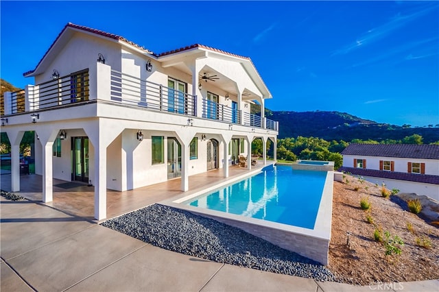 back of property featuring a patio, ceiling fan, a mountain view, and a balcony