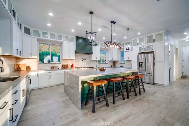 kitchen with appliances with stainless steel finishes, sink, light wood-type flooring, an island with sink, and light stone counters