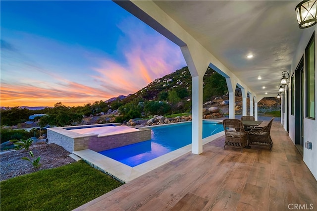 pool at dusk with an in ground hot tub and a patio